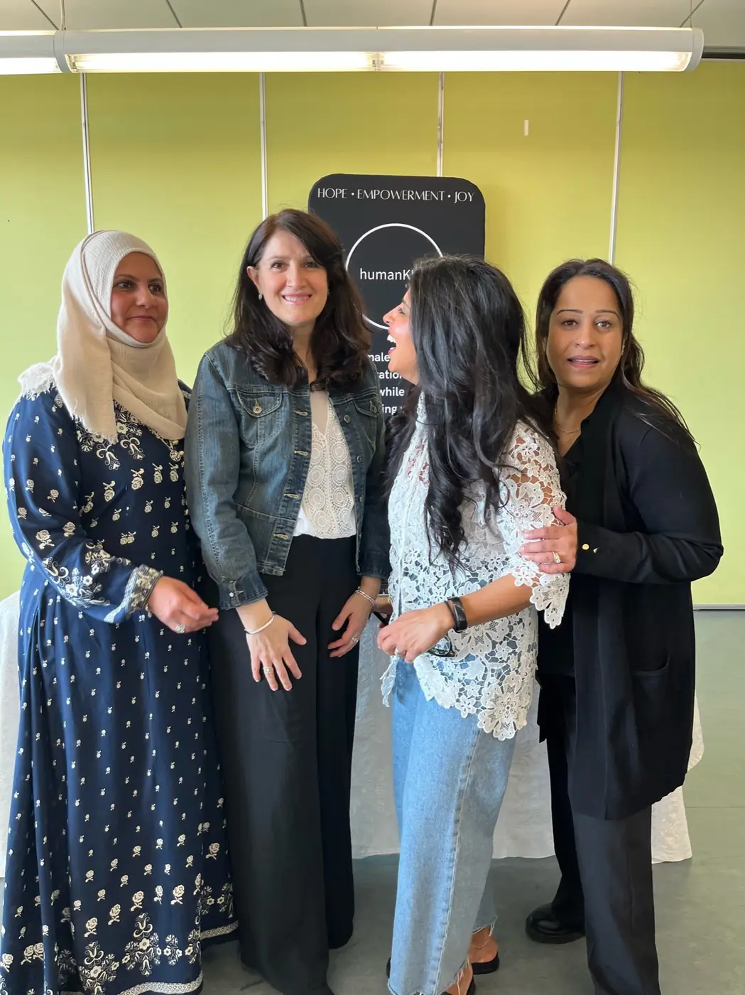 Four women from the humanKIND toronto community smiling together in front of the organization’s banner