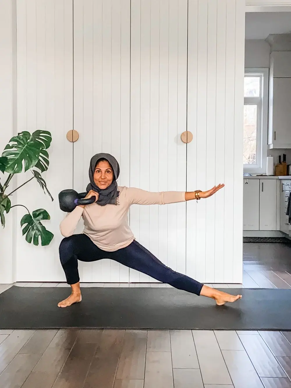 A woman in a deep lunge on a yoga mat holding a kettlebell