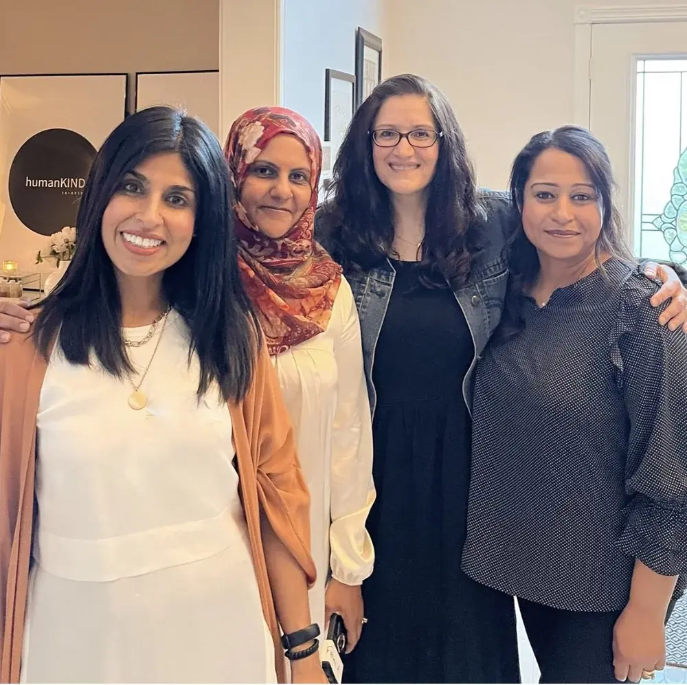 Four women smiling together in front of the humanKIND banner