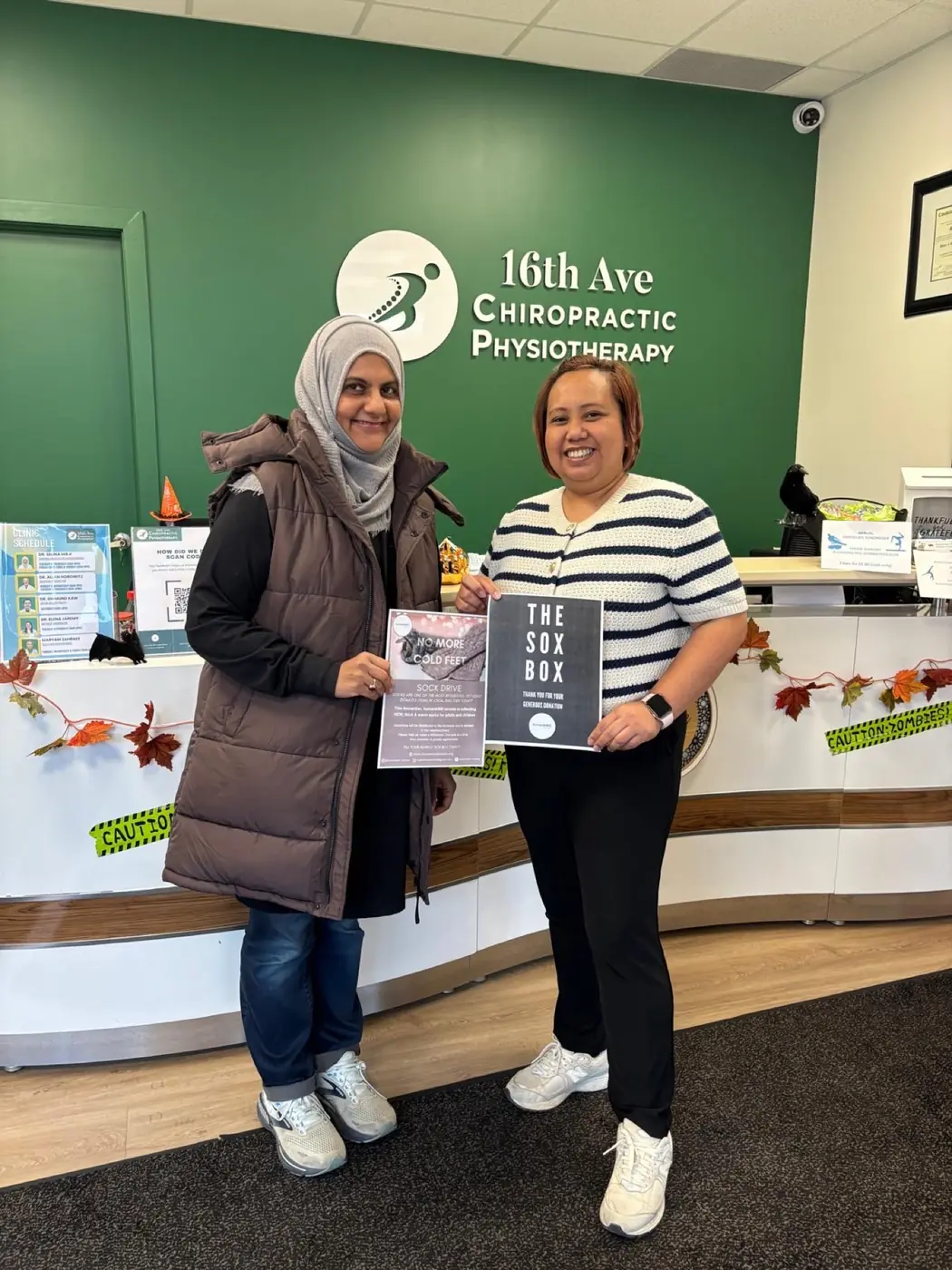 Two women at a local clinic holding a sign for the sock drive collection box
